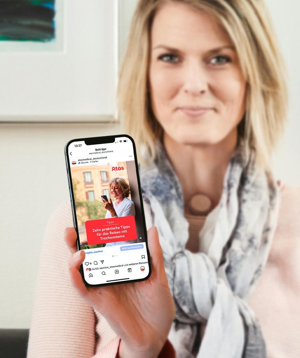 Atos Medical - Frau mit einem Halsstoma zeigt den Atos Instagram Kanal auf dem Handy