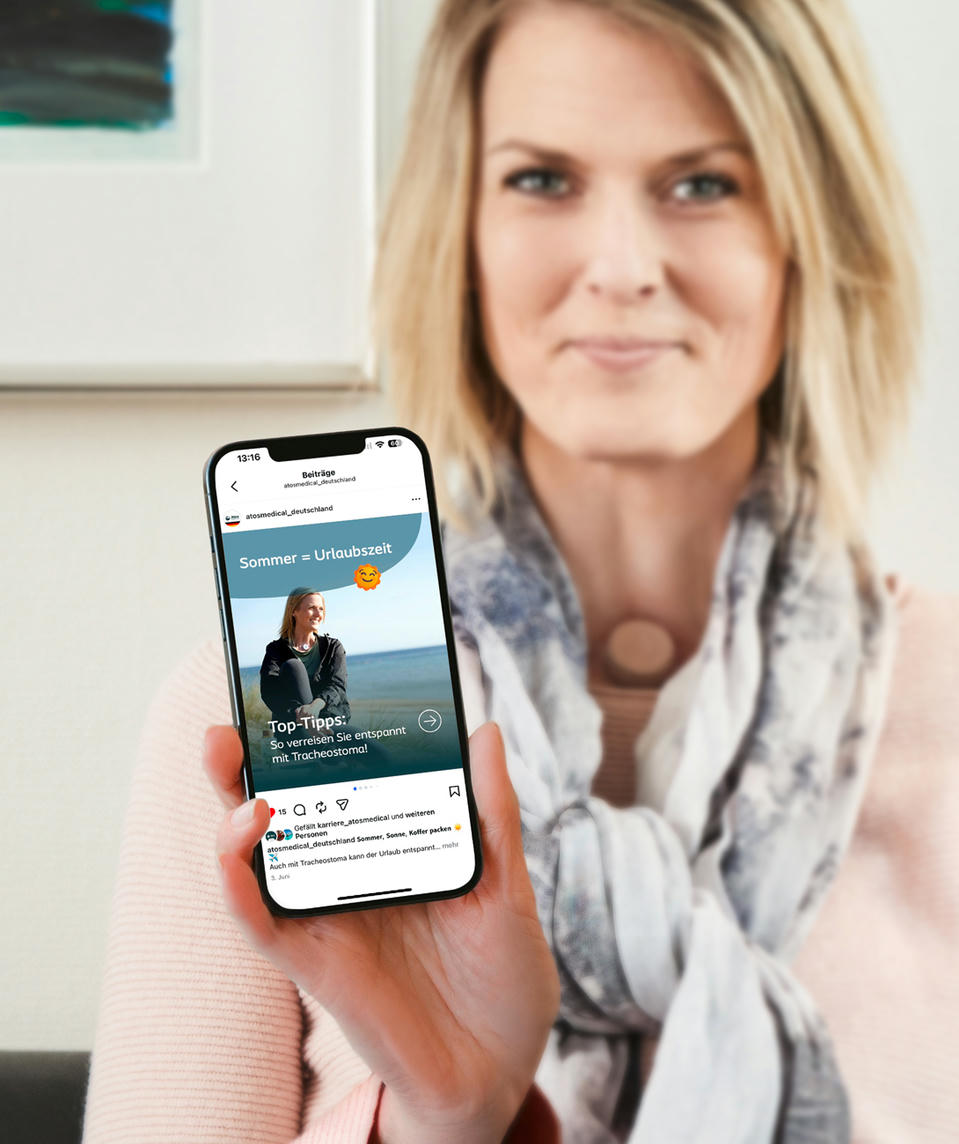 Atos Medical - Frau mit einem Halsstoma zeigt den Atos Instagram Kanal auf dem Handy