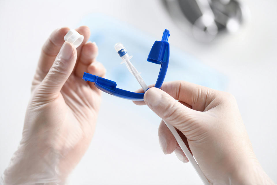 rechte und linke Hand in Hygienehandschuhen halten die Provox Vega Stimmprothese im Insertion System